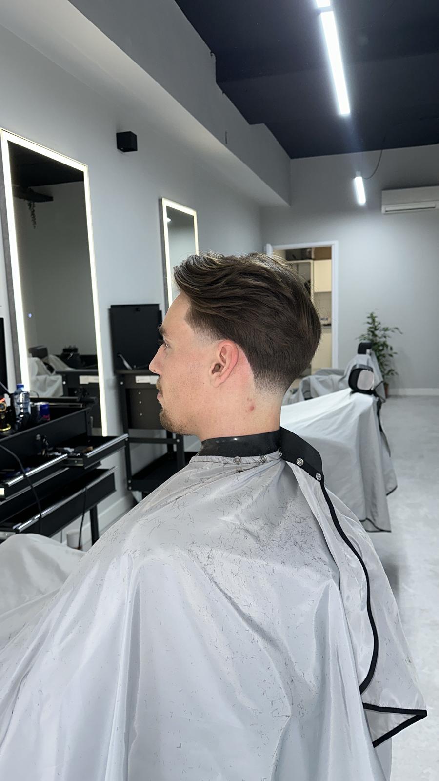 Klant met een mid fade en naar achteren gestyled bovenhaar, in de stoel bij Excellence Hair